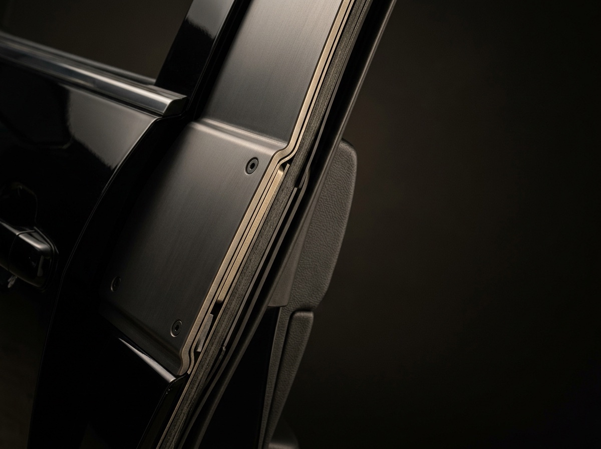 A brushed ballistic steel plate fastened along the door pillar, its machined edge stepped over the frame.