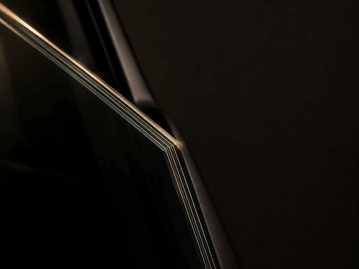 A single sheet of laminated ballistic glass seen edge-on, its interlayers traced by one rim light